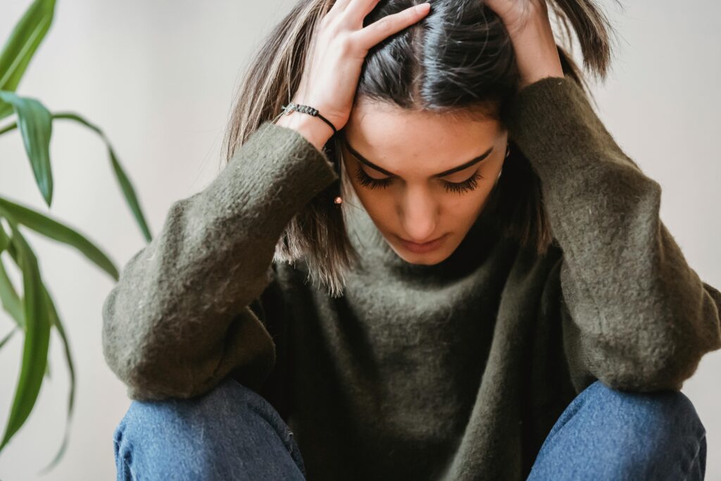 Woman experiencing misalignment burnout holding her head in her hands. Photo by Liza Summer: https://www.pexels.com/photo/depressed-young-ethnic-lady-touching-head-and-looking-down-sitting-near-wall-6382648/